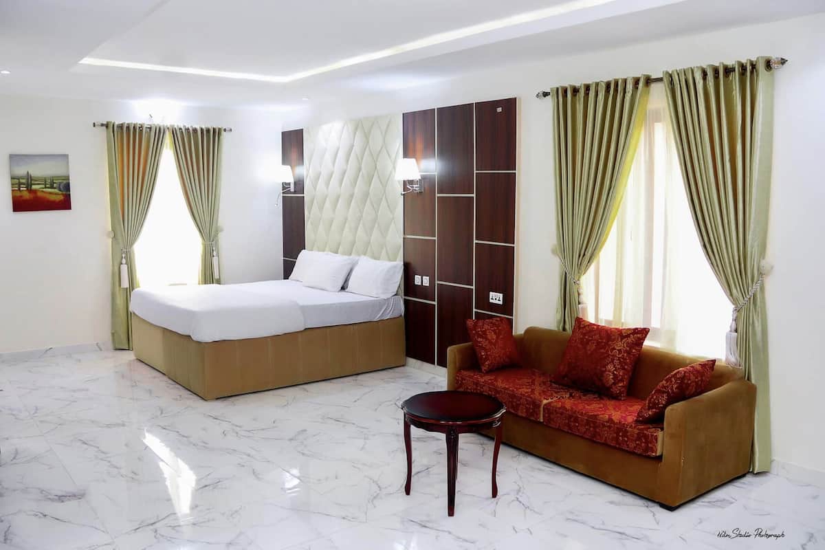 Quarto de hotel com cama, sofá, mesinha e cortinas.