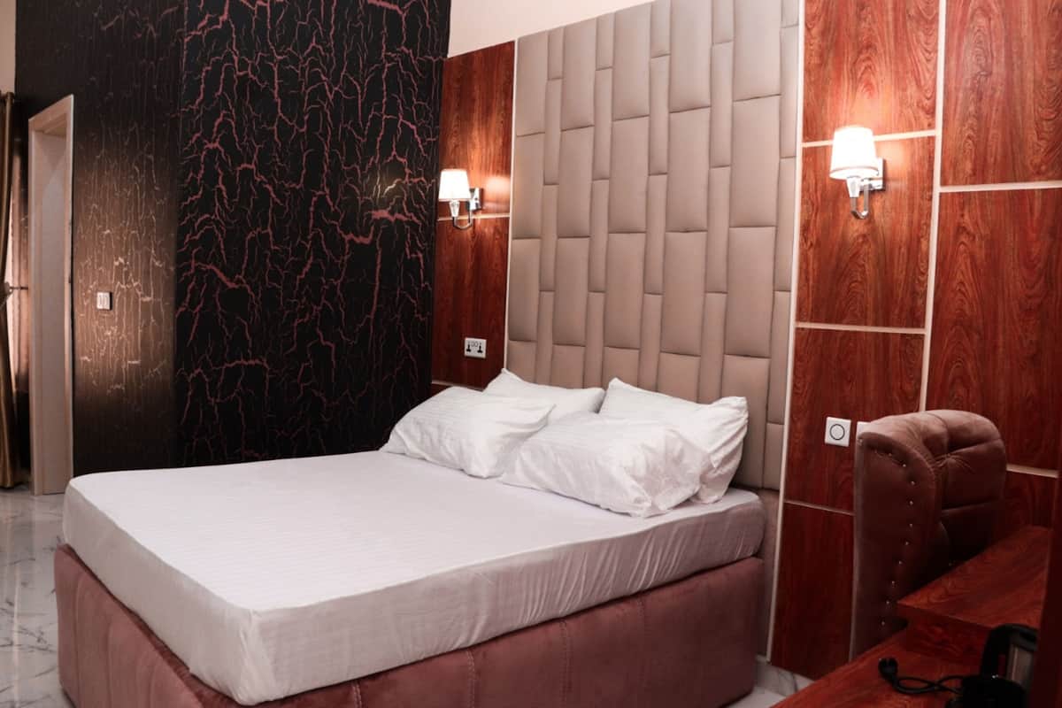 Um quarto moderno com uma cama grande, cabeceira com design acolchoado e duas luminárias fixadas na parede.