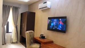 A room with a TV mounted on the wall, a wooden desk, a beige armchair, a wardrobe, and an air conditioning unit. - Ibom Waterfall Resorts and Suites (Arochukwu)