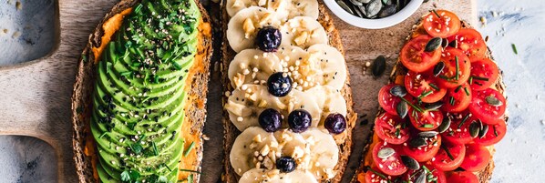 Three slices of toast with avocado, banana, and tomato toppings on a wooden board. - Ibom Waterfall Resorts and Suites (Arochukwu)