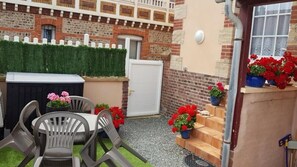 Un patio con mesa y sillas, un pequeño jardín de flores rojas y un muro de ladrillo con cerca blanca.