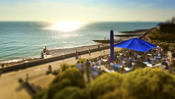 A beachside area with a crowd, a blue umbrella, and a view of the ocean.