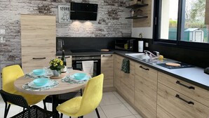 A modern kitchen with a brick wall, wooden cabinets, a dining table with yellow chairs, and a large window.