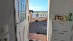 Eine geöffnete Tür, die zu einem Balkon mit weißem Zaun, einem blauen Eimer und einem kleinen Tisch mit Gegenständen darauf führt.