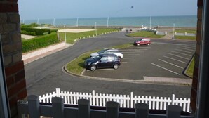 Ein Parkplatz mit Autos, einem weißen Zaun und Blick auf das Meer.