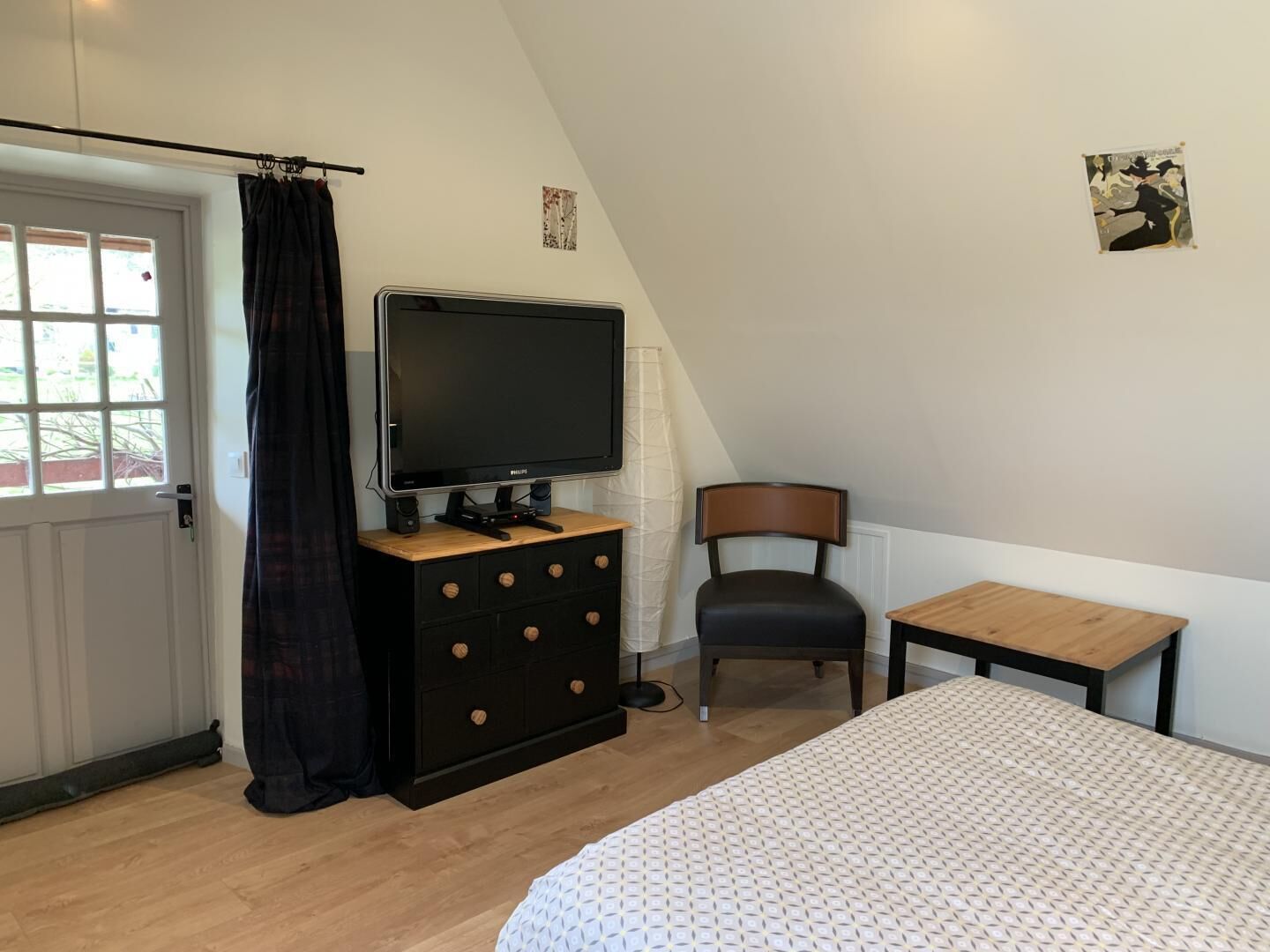 Ein Schlafzimmer mit einem Bett, einem Fernseher auf einer Kommode, einem Sessel und einem kleinen Tisch.