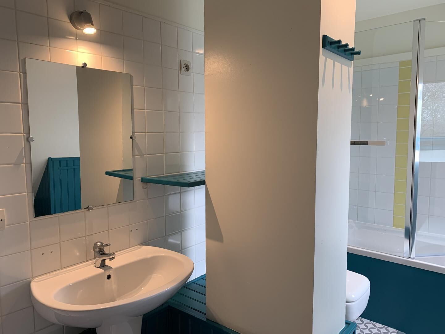 Un baño con lavamanos blanco, un espejo, un estante azul y zona de ducha.