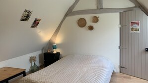 Un dormitorio con techo inclinado, una cama con colcha estampada, una mesita, una lámpara y una puerta con un letrero.