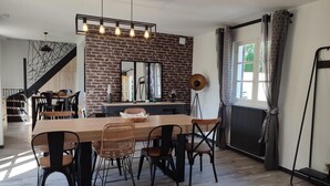 Un coin repas avec une table en bois et des chaises noires, un mur en briques et un grand miroir au-dessus de la table.