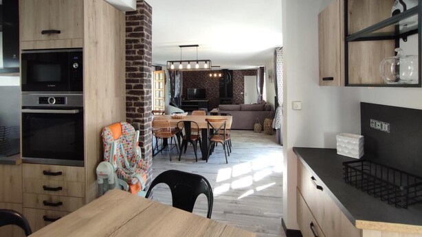 Une cuisine moderne dotée d’appareils électroménagers intégrés, un coin repas avec une table et des chaises en bois, et un espace de vie agrémenté d’une cheminée.
