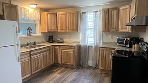 A kitchen with wooden cabinets, a refrigerator, a microwave, a stove, a sink, and a window with curtains.