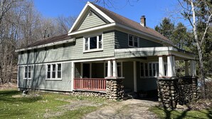 A two-story house with a stone foundation, a front porch, and a chimney.