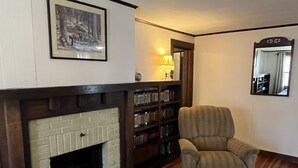 A cozy living room with a fireplace, a bookshelf, a comfortable armchair, and a mirror on the wall.