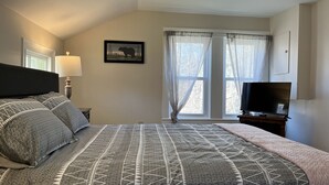 A bedroom with a bed, a TV, a lamp, a window with curtains, and a picture on the wall. - Calla Lily #2 - Oneonta Apartment close to downtown - 1 of 2 units (Oneonta)