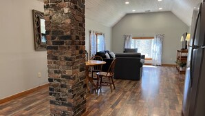 A spacious living area with a high ceiling, a fireplace, a dining table with chairs, a sofa, and a refrigerator. - Calla Lily #2 - Oneonta Apartment close to downtown - 1 of 2 units (Oneonta)