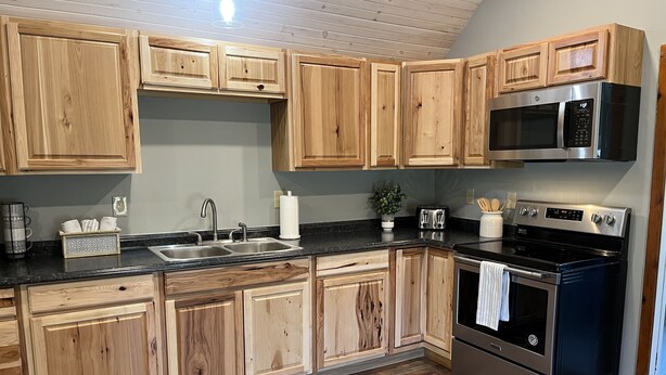 A kitchen with wooden cabinets, a stainless steel microwave, a toaster, and a black oven. - Calla Lily #2 - Oneonta Apartment close to downtown - 1 of 2 units (Oneonta)