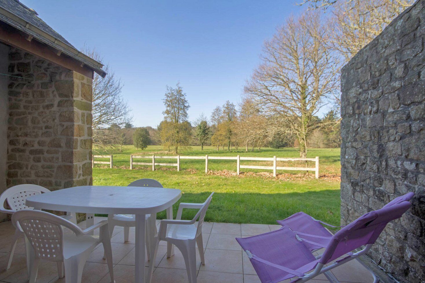A patio with a stone wall, a white table, and chairs.