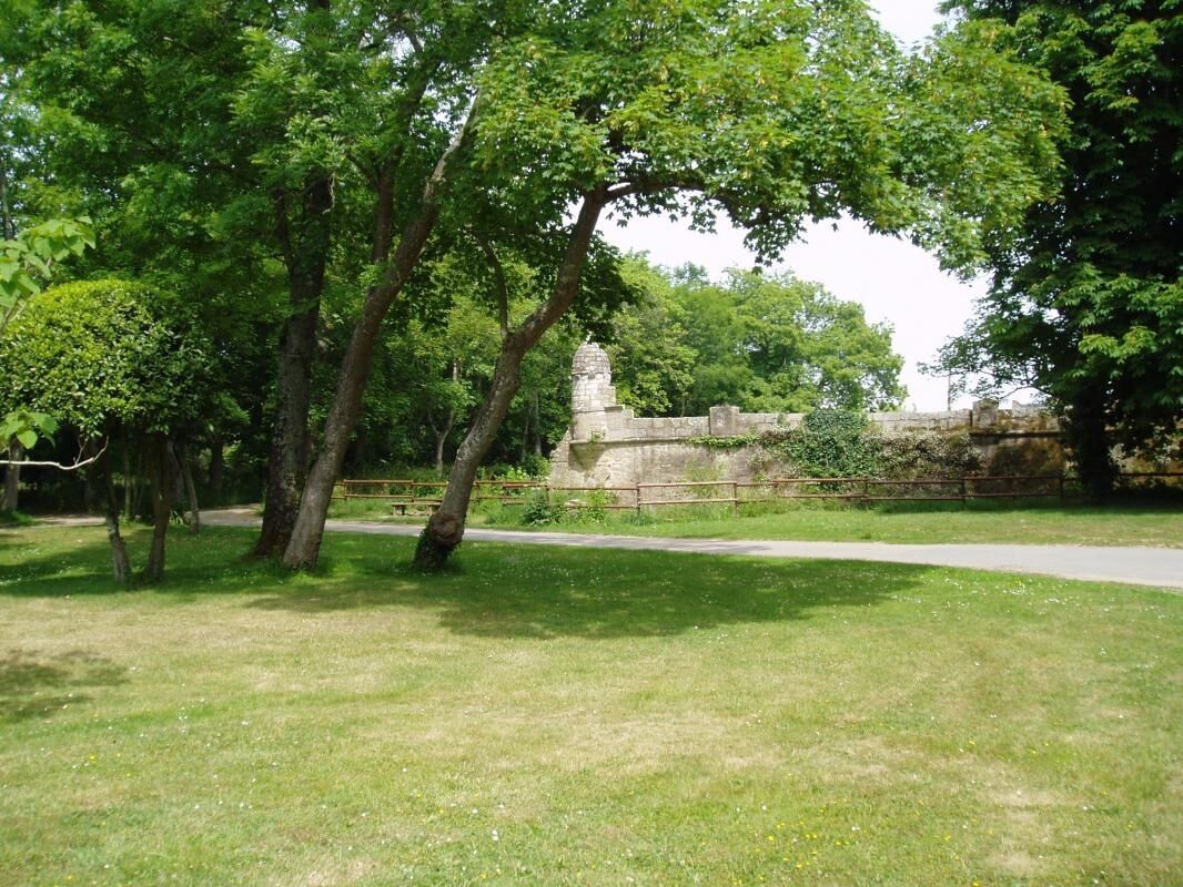 A park with trees, a stone wall, and a paved path.