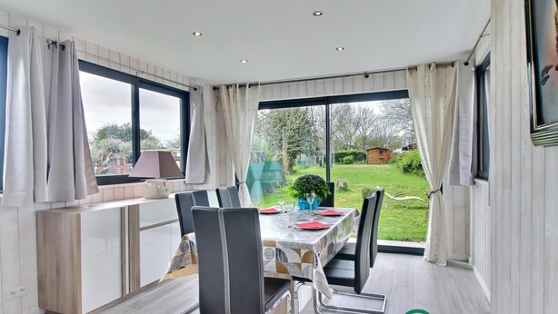 Un comedor con una mesa lista para dos personas, vistas al jardín y una zona de cocina con ventana.