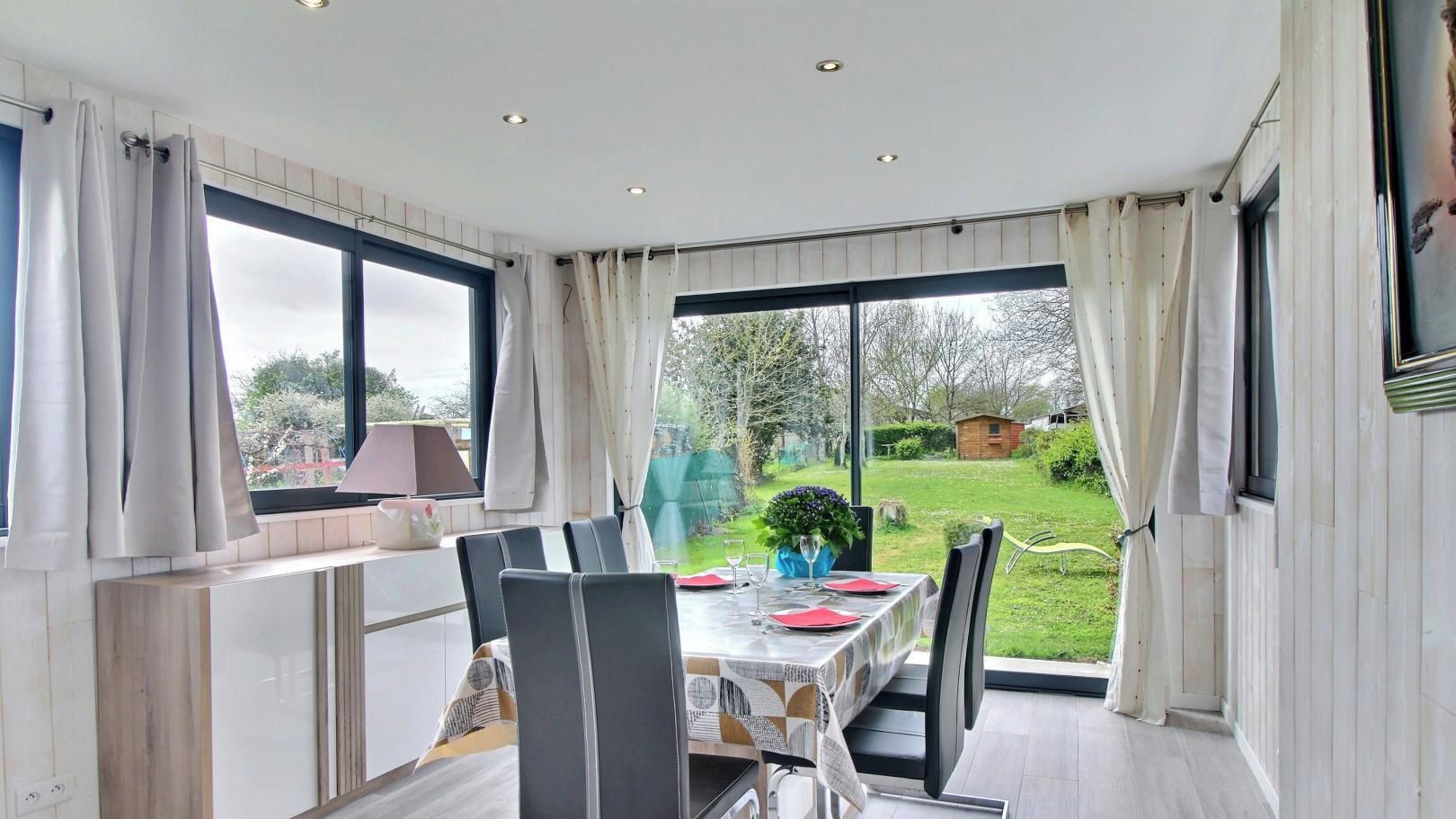 Een eethoek met een tafel voor twee, uitzicht op de tuin, en een keuken met een raam.