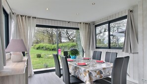 A dining area with a table set for six, large windows, and a view of the garden. - Du Pont Romain - Sarzeau (SARZEAU)