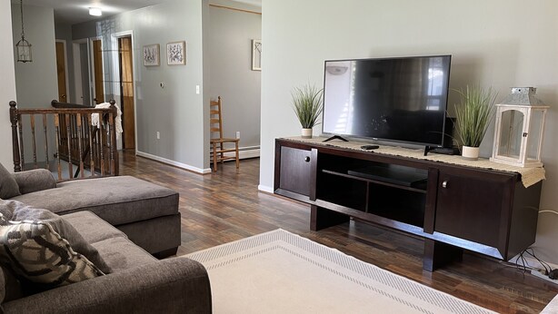 A living room with a dark wooden entertainment center, a large flat-screen TV, a grey sofa, and a white rug. - Patten Place - Close to everything in Oneonta - clean, updated private home. (Oneonta)