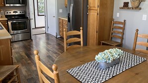 A kitchen with wooden cabinets, a stainless steel refrigerator, and a microwave. There is a dining table with chairs and a vase of flowers. - Patten Place - Close to everything in Oneonta - clean, updated private home. (Oneonta)