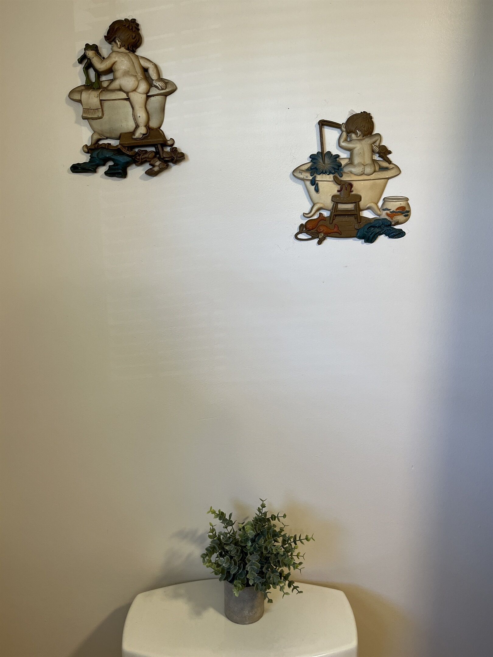 En væg med to dekorative metalfigurer og en lille potteplante.