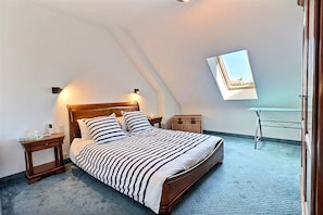 Un dormitorio con cama, mesitas de noche, una pequeña mesa y televisor instalado en la pared.
