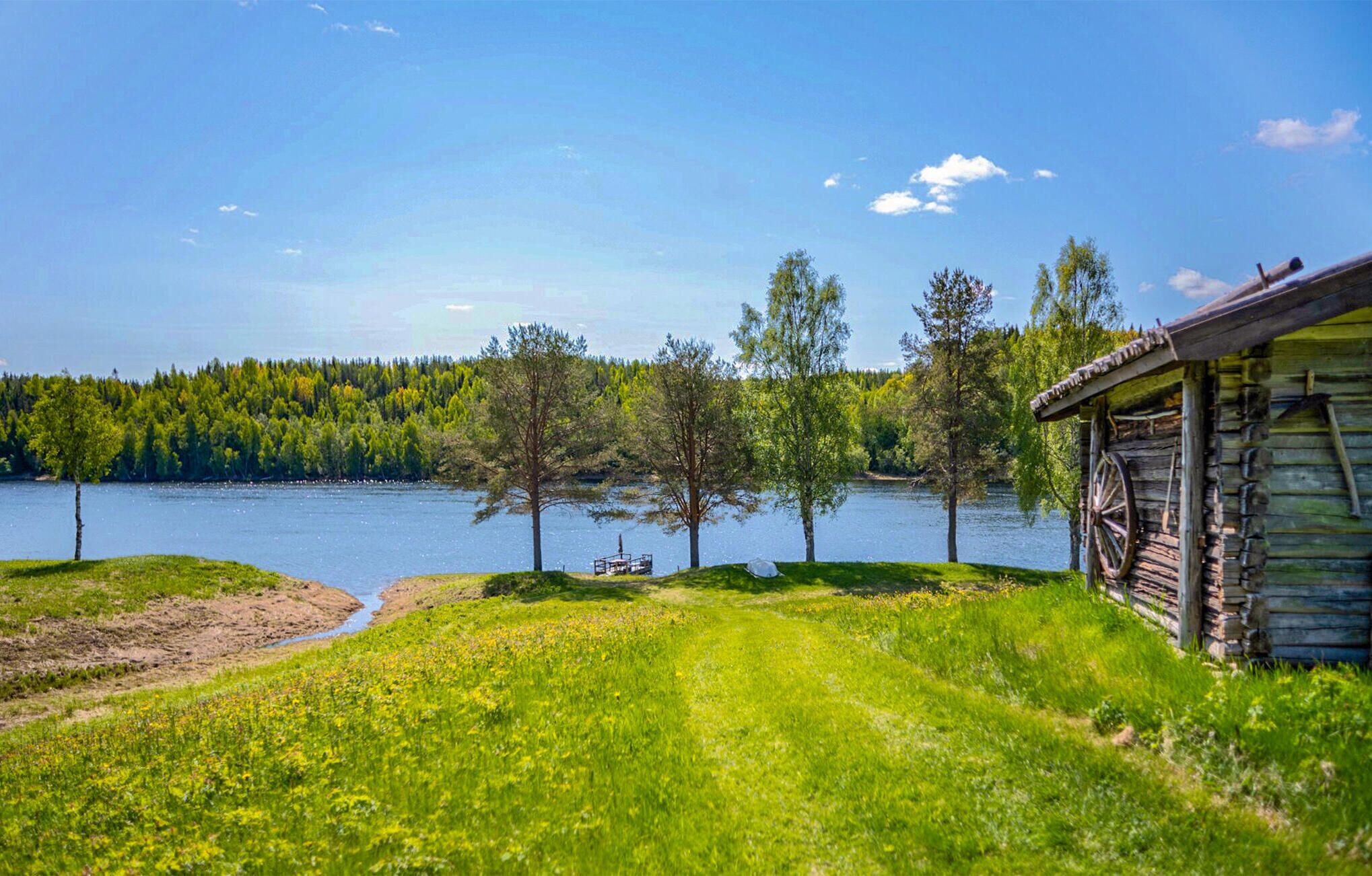 A cabin by a lake with a dock, surrounded by trees and grassy areas.