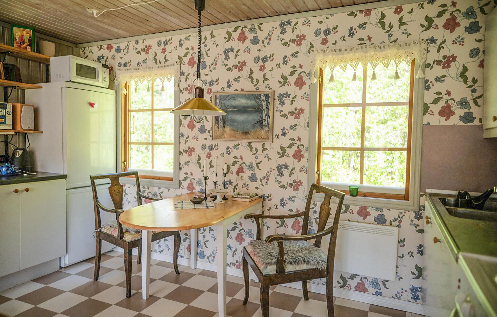 A kitchen with floral wallpaper, a wooden table, two chairs, and a hanging lamp.