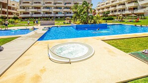 Una piscina grande al aire libre rodeada de jardines con palmeras y un jacuzzi en primer plano.