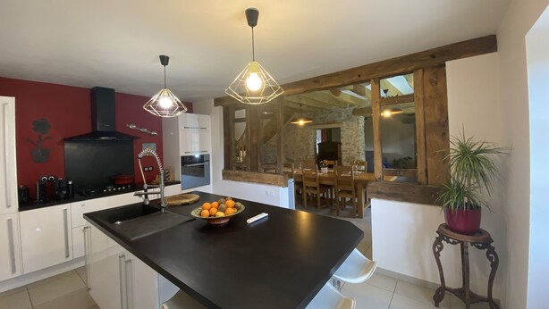 A modern kitchen with a central island, white bar stools, pendant lighting, and a dining area with a wooden table and chairs. - Longère *** with large heated swimming pool, sports room, billiards table, fibreglass in the countryside (La Roche-l'Abeille)