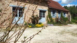 A stone house with a red-tiled roof, two windows with blue shutters, and a gravel driveway. - Longère *** with large heated swimming pool, sports room, billiards table, fibreglass in the countryside (La Roche-l'Abeille)
