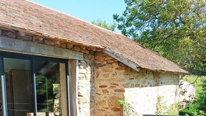 An outdoor patio area with wicker furniture, a stone building with a tiled roof, and a glass door leading to an interior space. - Longère *** with large heated swimming pool, sports room, billiards table, fibreglass in the countryside (La Roche-l'Abeille)