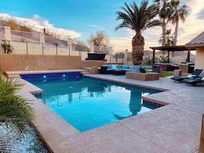 A swimming pool with a sunken seating area, surrounded by palm trees and a fenced patio.
