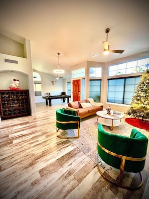 A spacious living room with a wooden floor, a green sofa, a green armchair, a coffee table, and a Christmas tree.