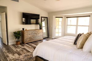 A bedroom with a large bed, a wooden dresser, a flat-screen TV, and a potted plant.