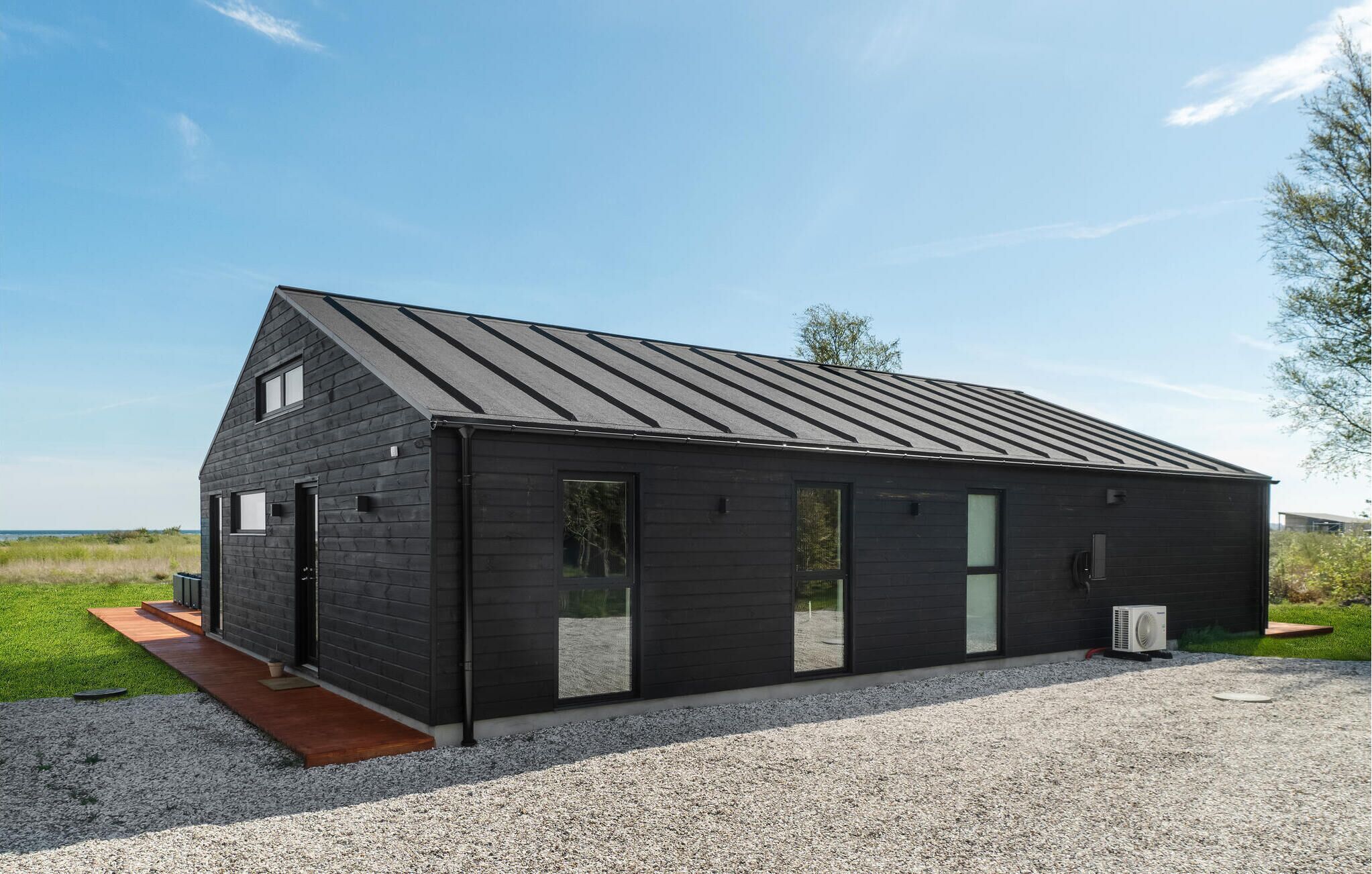 A modern, dark-colored building with a sloped roof, large windows, and a gravel driveway.