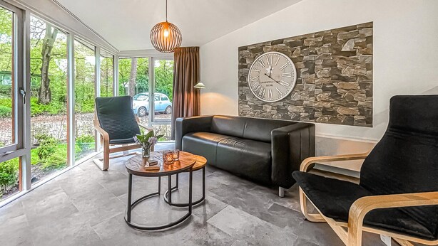 A modern living room with a black leather sofa, a wooden coffee table, and a stone wall clock.