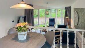 A dining area with a round table, chairs, a vase of flowers, and a view of the garden through large windows.
