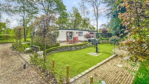 A mobile home with a fenced yard, a small patio with chairs, and a well-maintained lawn.