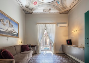 A room with a sofa, a table, a TV, and a patterned floor. - At the Résidences des Princes, past and present merge in a sense of everlasting excitement. (Catania)