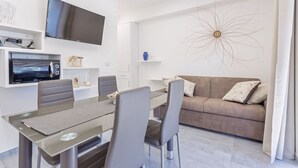 Ein modernes Wohnzimmer mit Flachbildfernseher, einem Esstisch mit Stühlen, einer Couch und einer Wanddekoration.