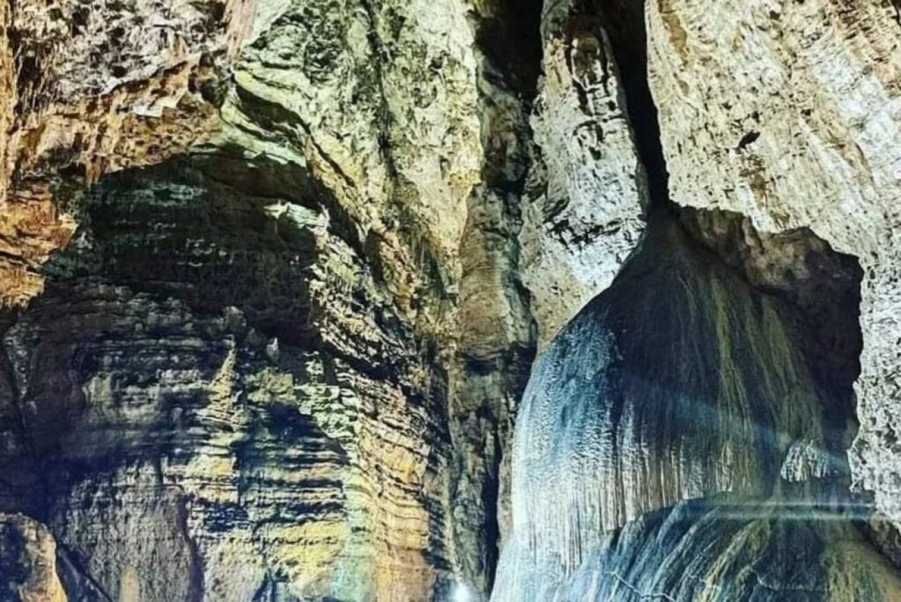 Interior de una cueva con formaciones rocosas estratificadas y una cascada.