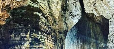 Interior de una cueva con formaciones rocosas estratificadas y una cascada.