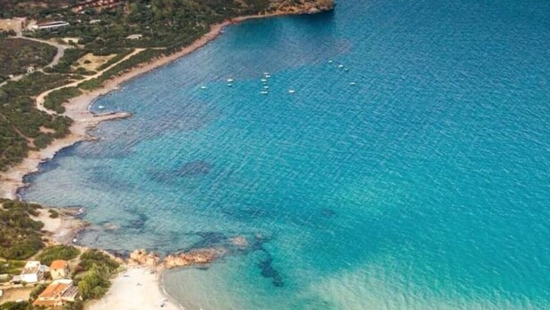 Luftaufnahme einer Küstenlandschaft mit Strand, klarem blauen Wasser und Booten.