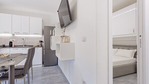 Eine moderne Küche mit weißen Schränken, ein Essbereich mit Tisch und Stühlen sowie ein Schlafzimmer mit Bett und Wand-Fernseher.