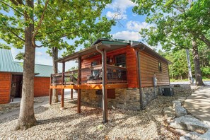 Une cabane en bois dotée d’un balcon, entourée d’arbres et reposant sur des fondations en pierre.