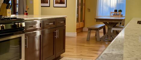 Una cocina con armarios de madera, una estufa y una zona de comedor con mesa y banco.